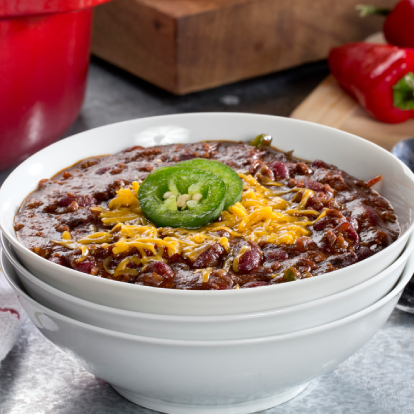 A bowl of chili topped with shredded cheese and a jalapeño slice.